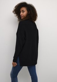 Schwarzer Strickpullover mit lockerer Passform, langen Ärmeln und gerippter Textur. Seitenschlitze und überschnittene Schultern unterstreichen das entspannte Design.