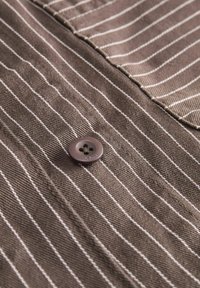 Brown striped fabric with a textured surface, featuring a single round button in a darker shade with four holes, sewn at the center.