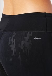 Leggings negros con un patrón texturizado, cinturilla alta y un pequeño logo "climalite" en la parte superior izquierda, fabricados con un tejido elástico.