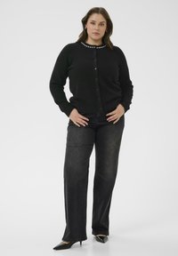 Cardigan noir en tricot avec un col rond, orné d'une bordure aspect perlé et d'une fermeture à boutons. Associé à un jeans droit noir et des talons noirs.