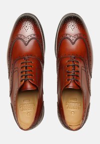 Braune Leder-Herrenschuhe im Wingtip-Design, mit durchbrochenen Details, gerundeten Zehen und einer Schnürung auf der Vorderseite. Strukturiertes Sohlenakzent.