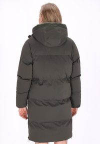 Sötétzöld puffermellény kapucnival, varrt panelek jellemzik, középhosszú szabású, és dupla oldalsó cipzárakkal rendelkezik a szellőzés és a könnyű mozgás érdekében.