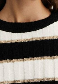 Sweter w czarno-białe paski o żebrowanej fakturze, z metalicznymi złotymi akcentami pomiędzy paskami. Okrągły dekolt.