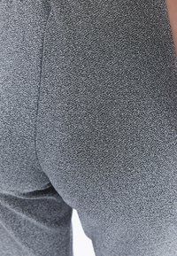 Grijze stof broek met een subtiel patroon, met een close-up afbeelding die de oppervlakte detail en vorm van het materiaal benadrukt.