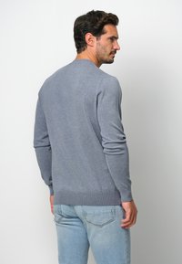 Maglione grigio realizzato in morbido tessuto, con colletto rotondo, maniche lunghe e orlo a costine. Indossato sopra jeans azzurri chiari.