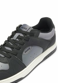 Czarne i szare sneakersy z teksturowaną syntetyczną cholewką, kontrastowymi panelami, okrągłym noskiem, płaskimi czarnymi sznurowadłami oraz białą gumową podeszwą. Zawierają akcenty z logo.