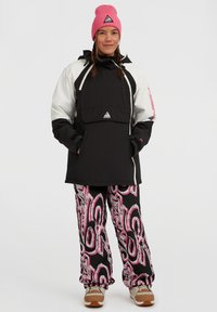 Zwart-witte geïsoleerde pulloverjack met een voork pocket, gecombineerd met roze en zwart patroon broek. Roze gebreide beanie met driehoeklogo.