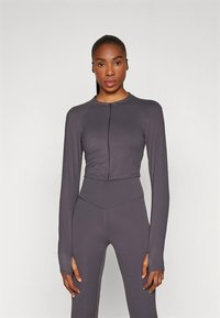 Casaco cinza comprido com zíper frontal, combinado com leggings de cintura alta combinando. Textura lisa, design atlético.