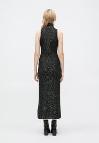 Black, knitted, sleeveless dress with a high neck. Features a fitted silhouette and sparkly silver accents. Mid-calf length with a straight hem.