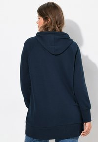 Felpa con cappuccio blu navy, dal fitting rilassato, maniche lunghe raglan, orlo a costine e tessuto morbido. Include una tasca a marsupio.