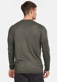 Pull vert olive à manches longues avec une texture côtelée, col rond et poignets ajustés. Présente une coupe standard et des détails de couture subtils.