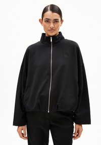 Schwarze Zip-Up-Sweatjacke mit hohem Kragen, lockerer Passform und elastischem Saum. Verfügt über ein dezentes Logo auf der linken Brust. Weicher Stoff.