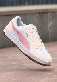 Hvide og lyserøde lædersneakers med perforeret tåboks, gummisål og en guldsymbolaccent på siden. Glatte og teksturerede detaljer.