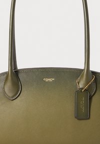 Olive green leather handbag with smooth texture, dual handles, and gold-tone hardware. Features a hanging tag and embossed logo.