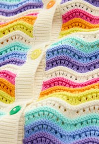 Gilet en tricot avec des rayures ondulées aux couleurs pastel : rose, orange, jaune, vert, bleu et violet, soulignées par des boutons crème.