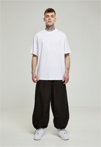 Hvid oversized t-shirt parret med løse sorte bukser og hvide sneakers. Stoffet ser glat ud, med en afslappet pasform og et afslappet design.