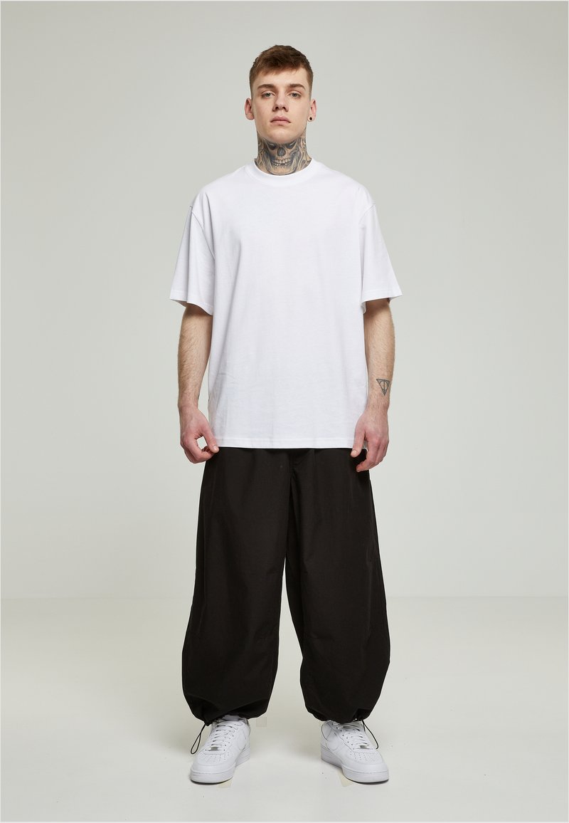 Hvid oversized t-shirt parret med løse sorte bukser og hvide sneakers. Stoffet ser glat ud, med en afslappet pasform og et afslappet design.