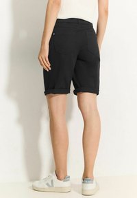 Schwarze Jeansshorts mit umgeschlagenem Saum, zwei Gesäßtaschen und glatter Textur. Kombiniert mit weißen Turnschuhen und einem enganliegenden Oberteil.