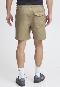 Shorts kaki avec une ceinture élastique et une poche arrière avec bouton. Le tissu a une texture lisse, adaptée à un usage décontracté.