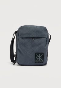 Γκρι τσαντάκι ώμου από νάιλον με γεωμετρικό σχέδιο, κλείσιμο με φερμουάρ, μπροστινή τσέπη και μαύρο εμπριμέ λογότυπο Calvin Klein. Περιλαμβάνεται ρυθμιζόμενο λουράκι.