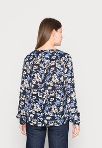 Blusa floral de mangas longas em azul-marinho, com flores brancas e azuis claras e um decote redondo, feita de tecido leve.