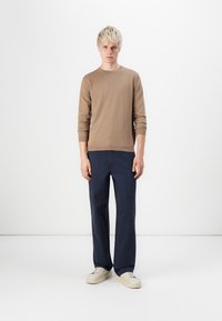 Brown long-sleeve sweater with a crew neckline, paired with navy blue trousers. White sneakers complete the outfit. Simple, fitted design.