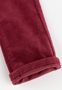 Burgunderfarbene Cordhose mit weichem Material, eines umgeschlagenen Saums und sichtbaren vertikalen Rillen im Stoff.