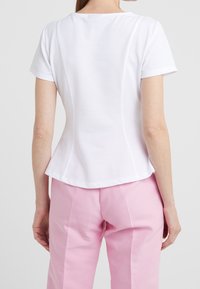 Hvid kortærmet top i textureret stof, med rund halsudskæring og buede sømdetaljer bagpå, parret med pink bukser.