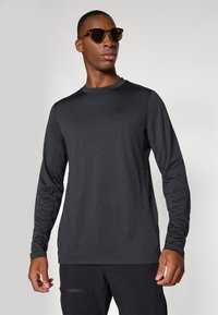 Langärmliges schwarzes Sportshirt aus leichtem Stoff, mit rundem Ausschnitt und dezentem Logo auf der Brust, kombiniert mit braunen Sonnenbrillen.