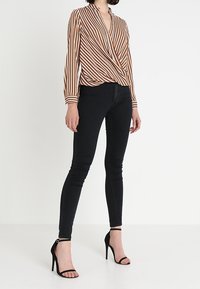 Blouse cache-cœur à rayures marron, orange et crème, associée à un jean skinny noir et des sandales à talons aiguilles noires. Caractérisée par des manches longues et un décolleté en V.