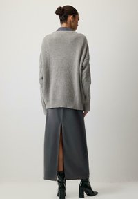 Pelēka adīta džemperis ar kabelīšu rakstu, apvienots ar tumši pelēku, līdz ceļgaliem garu svārku ar aizmugurēju šķēlumu. Modelei kājas melnas potīšu zābakus.