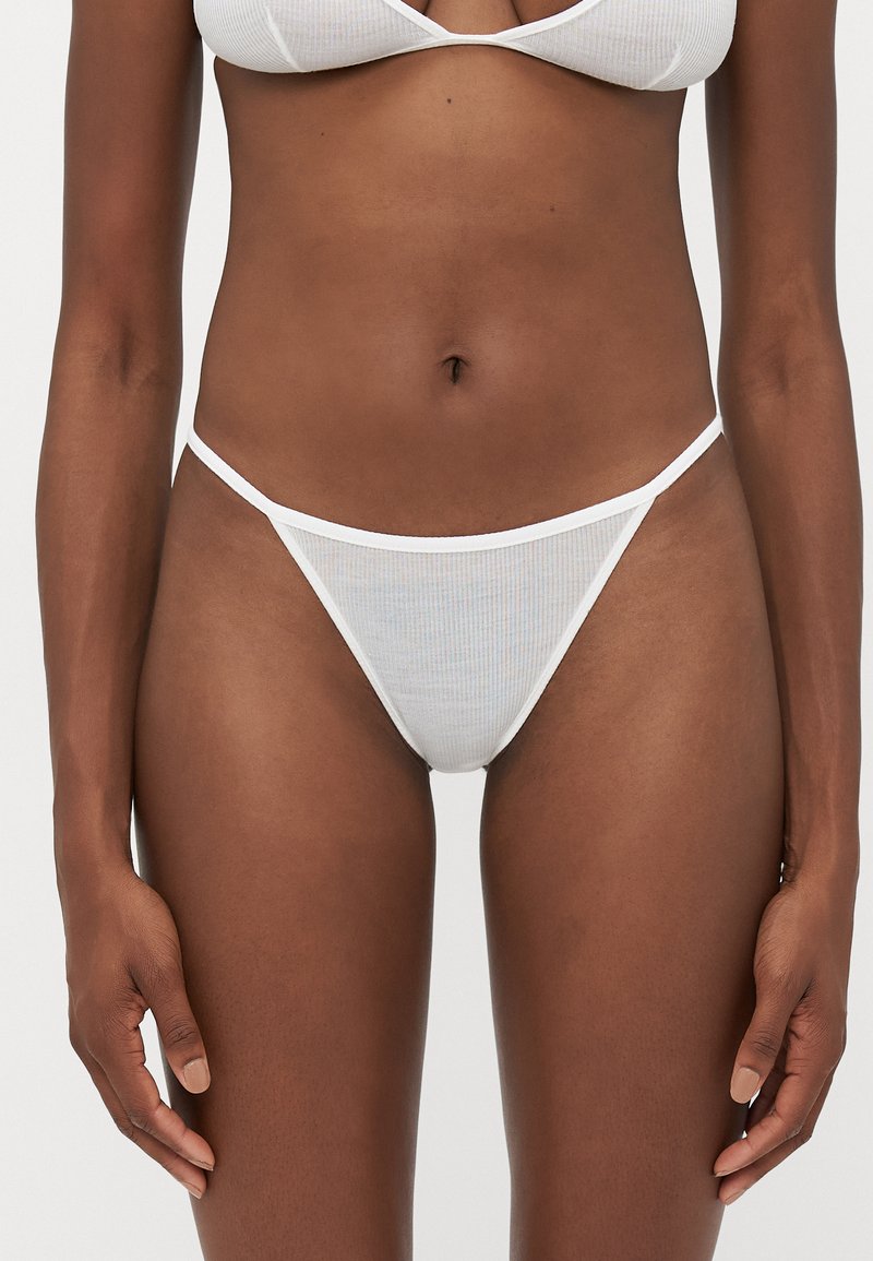 Baltā ribota bikini apakšdaļa ar plānām sānu siksnām, kas piedāvā caurspīdīgu tekstūru. Vienkāršs dizains ar minimālistisku un mūsdienīgu estētiku.