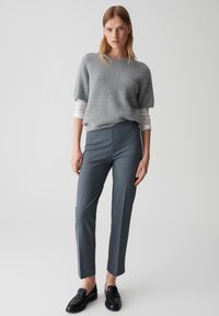 Lichtgrijze fuzzy trui, witte lange mouwen shirt eronder, slanke donkergrijze op maat gemaakte broek en zwarte loafers, tegen een neutrale achtergrond.