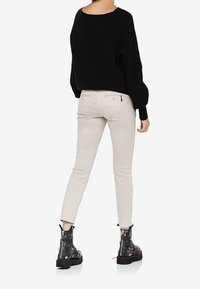 Svart stickad tröja med vid halsringning, beige åtsittande byxor och blommiga snörstövlar med chunky sula.