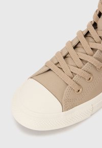 Beige vászon magas szárú sneaker lapos fűzővel, gumírozott lábujjrésszel, texturált felülettel és diszkrét varrási részletekkel. Az alsó részen gyémánt mintázat található.