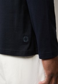 Navy short-sleeve T-shirt featuring a slim fit, cotton material, and a subtle cross emblem at the hem. Smooth texture with neat stitching.
