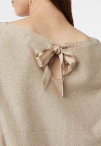 Beżowy sweter z dzianiny z tylnym otworem zapinanym na satynową wstążkę. Miękka tekstura z prążkowanym dekoltem i subtelnym połyskiem.