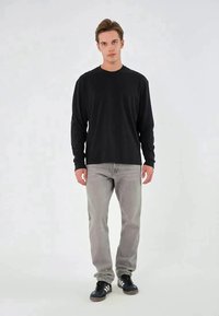 Zwart shirt met lange mouwen en een ronde hals, gecombineerd met lichtgrijze jeans en zwarte sneakers. Gladde stof met een casual pasvorm.