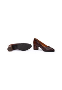 Une paire de chaussures à talons blocs bas pour femmes en cuir brun, l'une montrant le dessus et l'autre la semelle avec un grip texturé et un talon en bois.