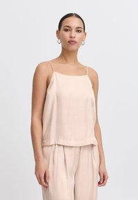 Vaalea beige silkki-hihaton paita, jossa on ohuet hihnat, neliömainen pääntie ja löysä istuvuus. Huomattava sileä rakenne ja hienovarainen kiilto.