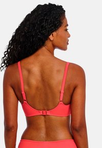 Coral underwire bra with adjustable straps, smooth texture, and a clasp closure at the back. Minimalist design, no visible patterns.