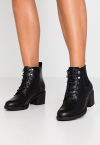 Bottines en cuir noir à bout rond, à lacets à l'avant et à talon carré. Comprend des œillets en métal argenté et une fermeture éclair sur le côté pour un enfilage facile.