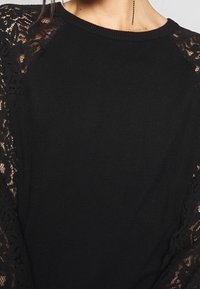 Zwart topje met kanten mouwen, een ronde halslijn en een aansluitend ontwerp. De stof is zacht met ingewikkelde kanten details en een contrasterende textuur.