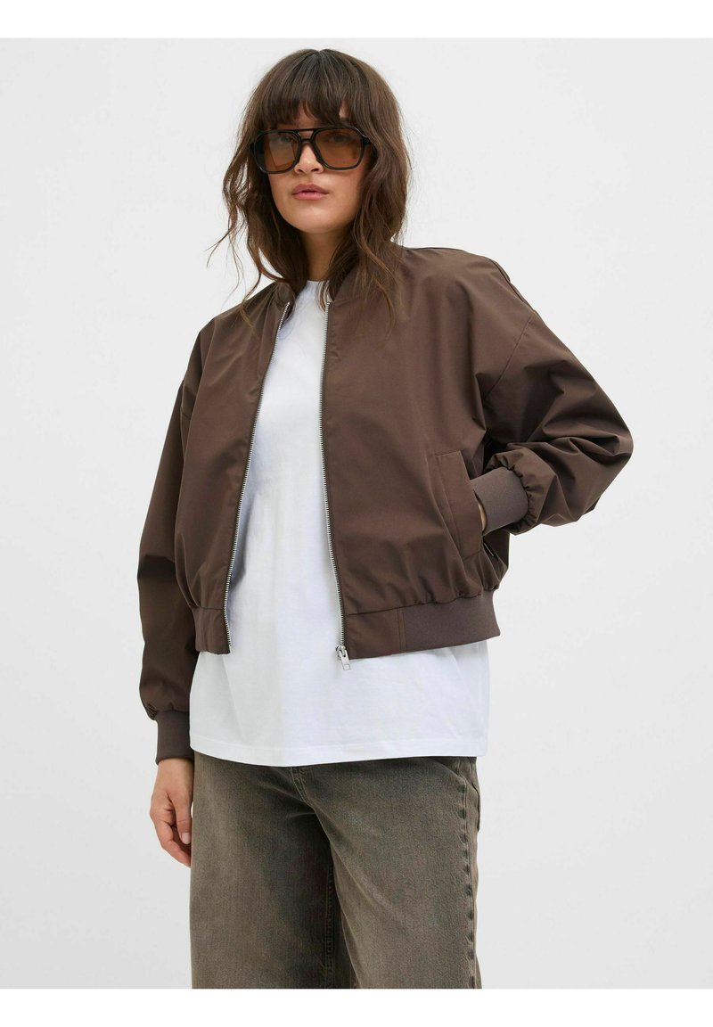 Bruine bomberjack met een ritssluiting aan de voorkant, geribde manchetten en zoom. Draag het over een witte T-shirt, gecombineerd met olijfgroene, vervaagde broeken.