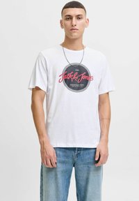 Witte katoenen t-shirt met een ronde zwarte en rode grafische logo, korte mouwen en een ontspannen pasvorm, gecombineerd met lichtblauwe denim jeans.
