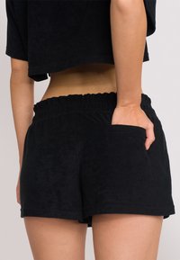 Pantaloni shorts in terry nero con vita elasticizzata e tasca laterale. I pantaloni shorts hanno una vestibilità comoda e una texture liscia.