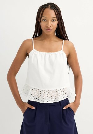 Top sin mangas blanco con escote fruncido y dobladillo de peplum de encaje de ojal, combinado con pantalones azul marino. Telas suaves con textura delicada.