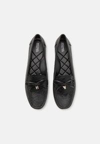 Mocassins en cuir noir avec une finition texturée, présentant une semelle intérieure matelassée, un détail en nœud et un accent argenté à l'avant.