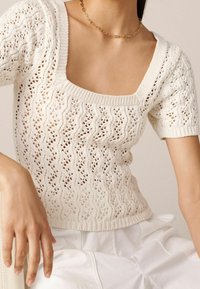 Hvid strikket sweater med firkantet udskæring, korte ærmer og bølgemønster. Har en ribbestrikket kant og et tekstureret, åbent vævning design.