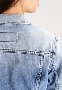 Ljusblå denimjacka med en klassisk design, synliga sömmar, en enkel baksida och en något sliten textur.